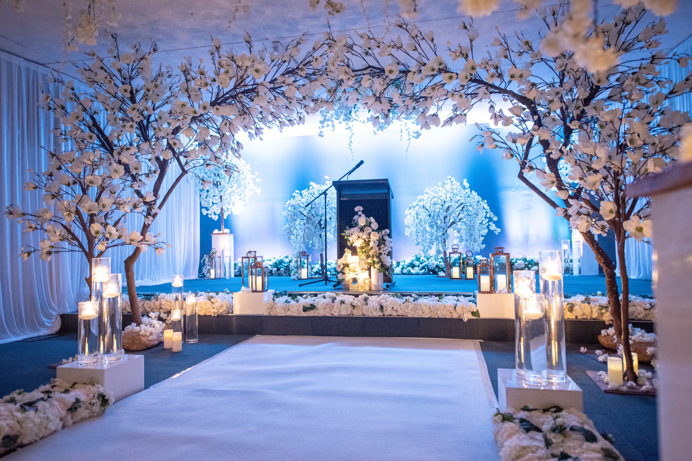 White floral wedding ceremony setting with a candlelit aisle and lectern