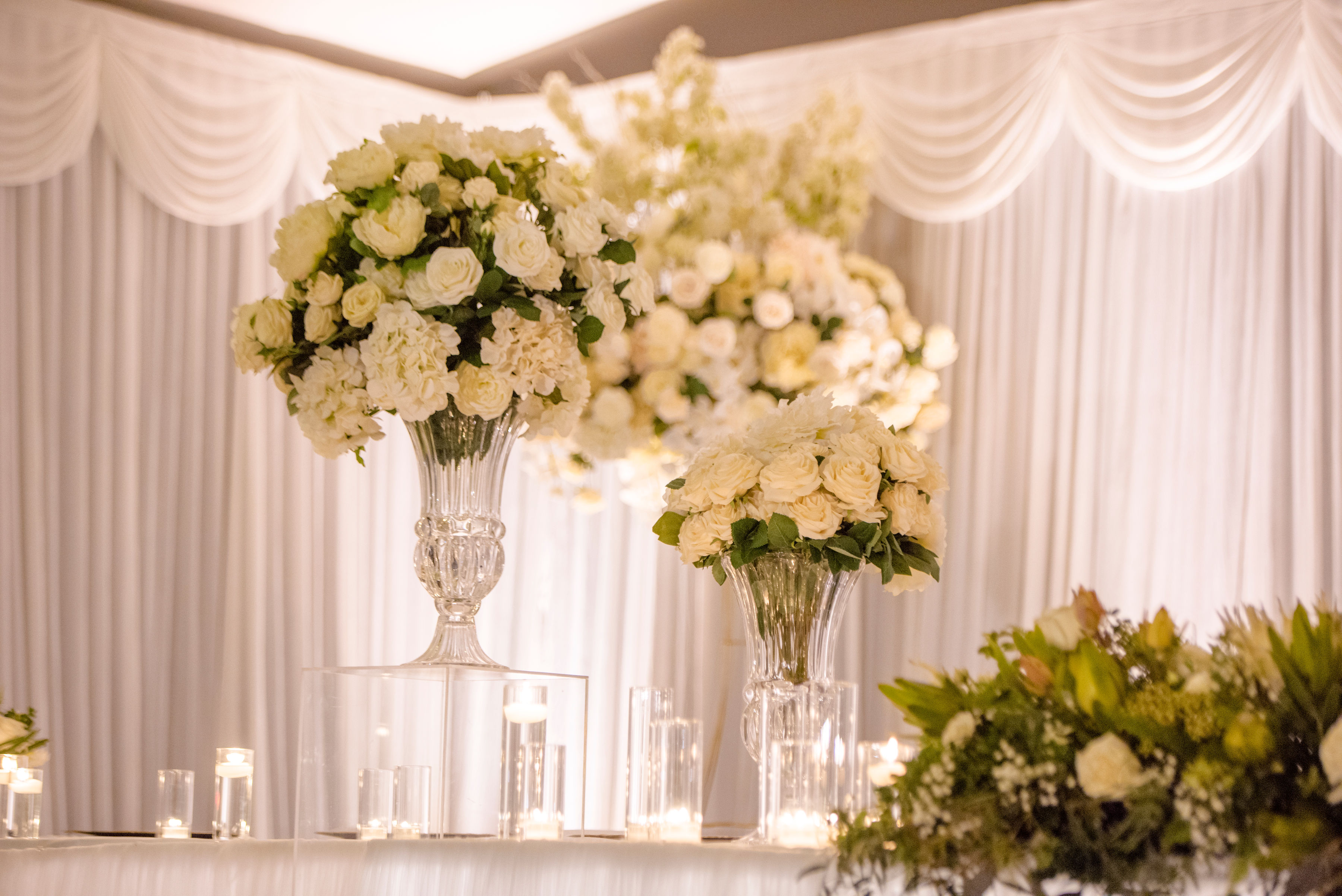 White floral arrangements in glass vases against a draped backdrop
